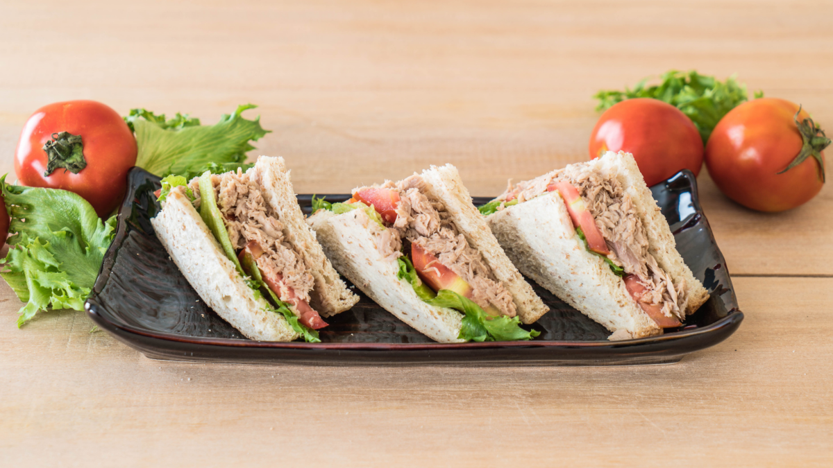 A delectable trio of freshly made sandwich slices, layered with tender tuna, crisp lettuce, and ripe tomatoes, served on a sleek black platter, surrounded by vibrant tomatoes and greens that add a touch of freshness to any meal setting. Image Credit: topntp/ 123RF