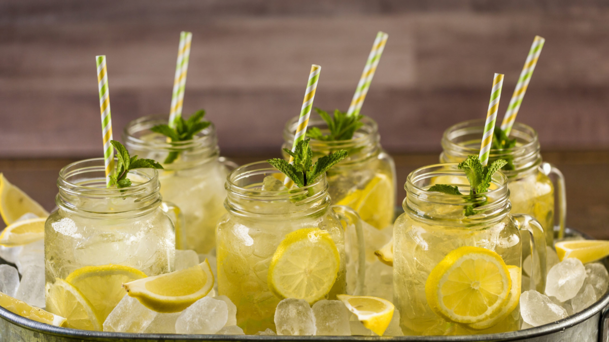 A refreshing summer gathering awaits with mason jars filled with zesty lemonade, adorned with fresh mint and vibrant lemon slices, perfectly chilled over a bed of ice. Sipped through colorful straws, this scene invites friends to enjoy cooling moments under the sun. Image Credit: arinahabich/ 123RF