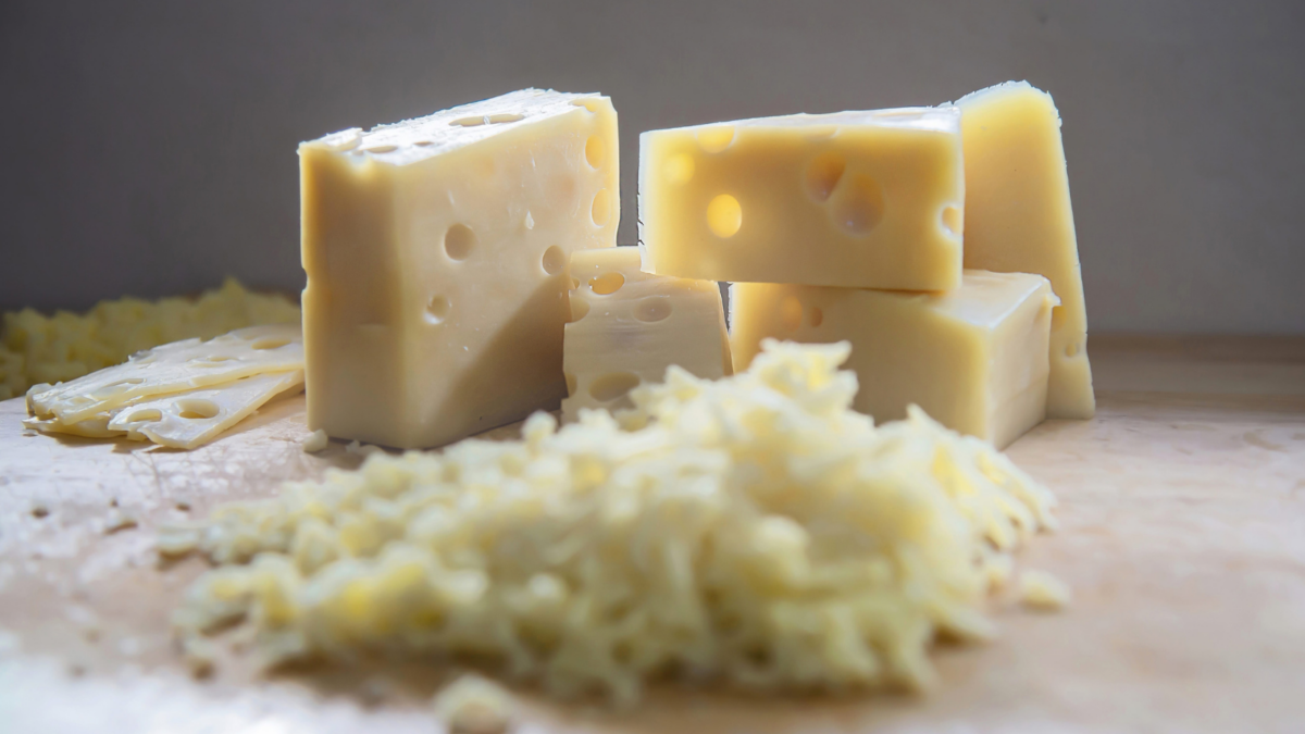 A delectable arrangement of cheese chunks and shavings, perfect for a culinary masterpiece. The creamy texture and holes invite you to savor every bite, while the scattered shavings hint at a dish in the making, waiting for flavor and creativity to blend.