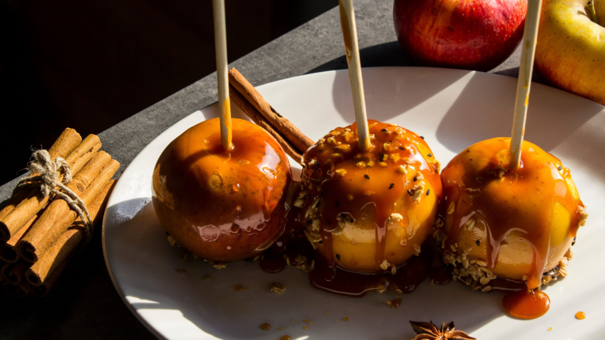 Indulging in a delightful autumn treat, three caramel-coated apples sit beautifully on a plate, surrounded by cinnamon sticks and fresh apples, creating a perfect mix of fall flavors. Image Credit: mayashustov/ 123RF