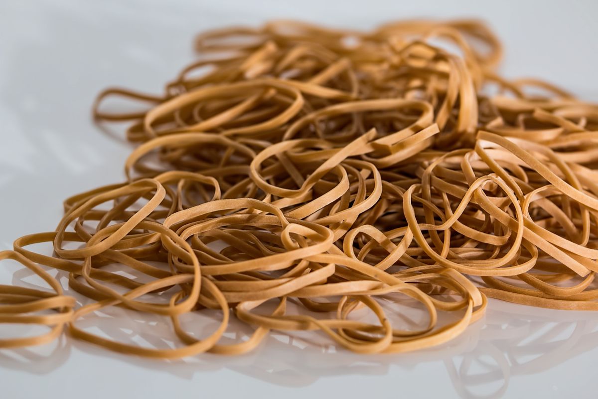10 Things Boomers Always Kept in the Kitchen Junk Drawer 1 A close-up image of a scattered pile of brown rubber bands on a reflective surface.