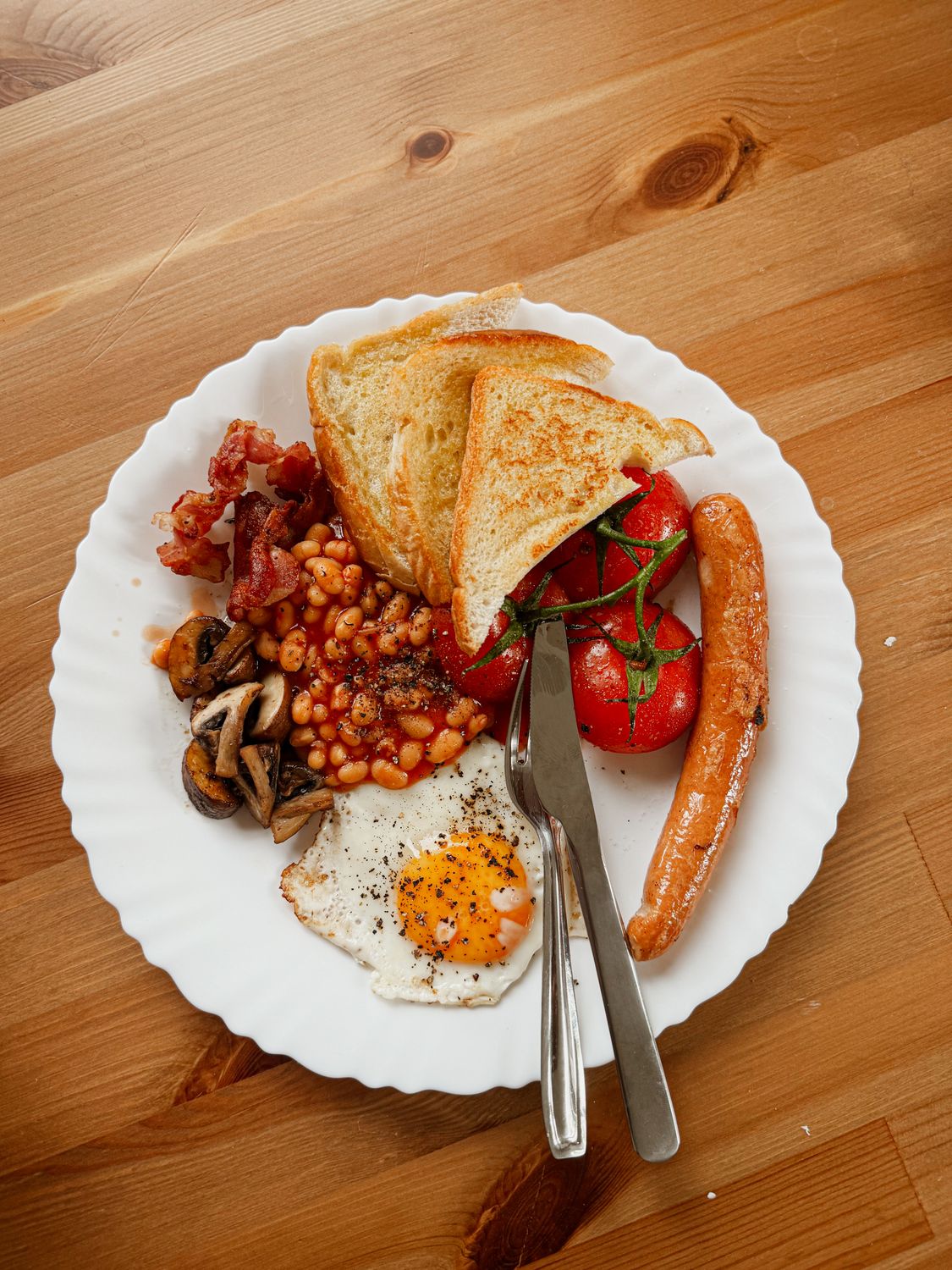 A delicious full English breakfast featuring eggs, sausage, beans, and toast on a wooden table.