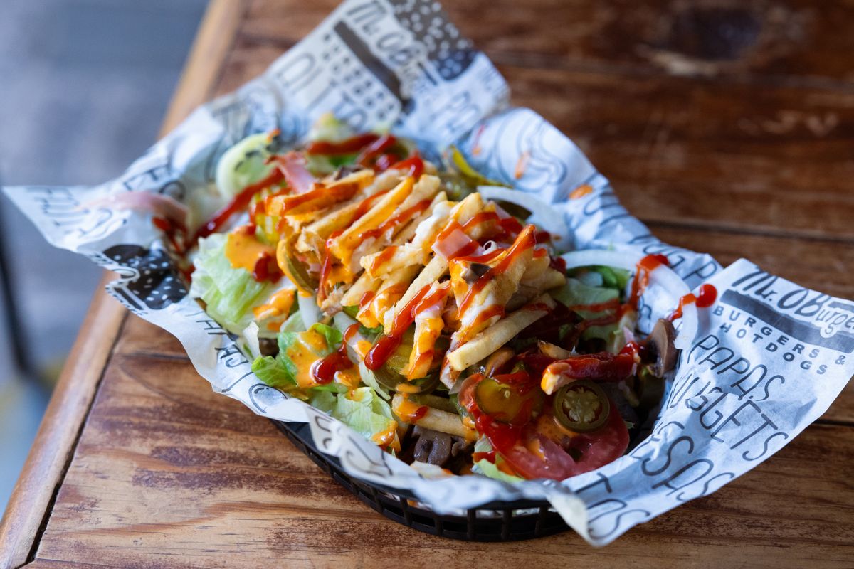 A delicious serving of loaded fries with toppings, served in a paper-lined basket, perfect for a casual dining setting.