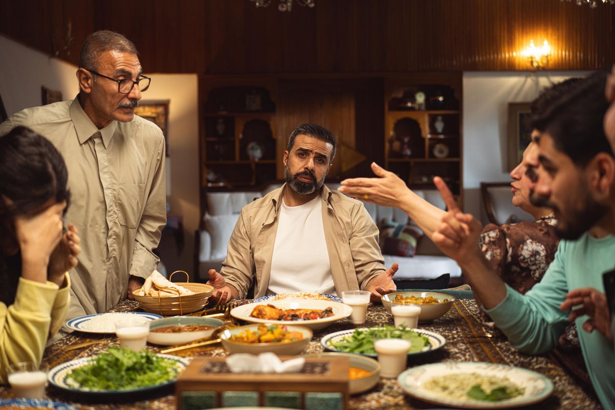 A family engages in a lively discussion around a dinner table filled with dishes.