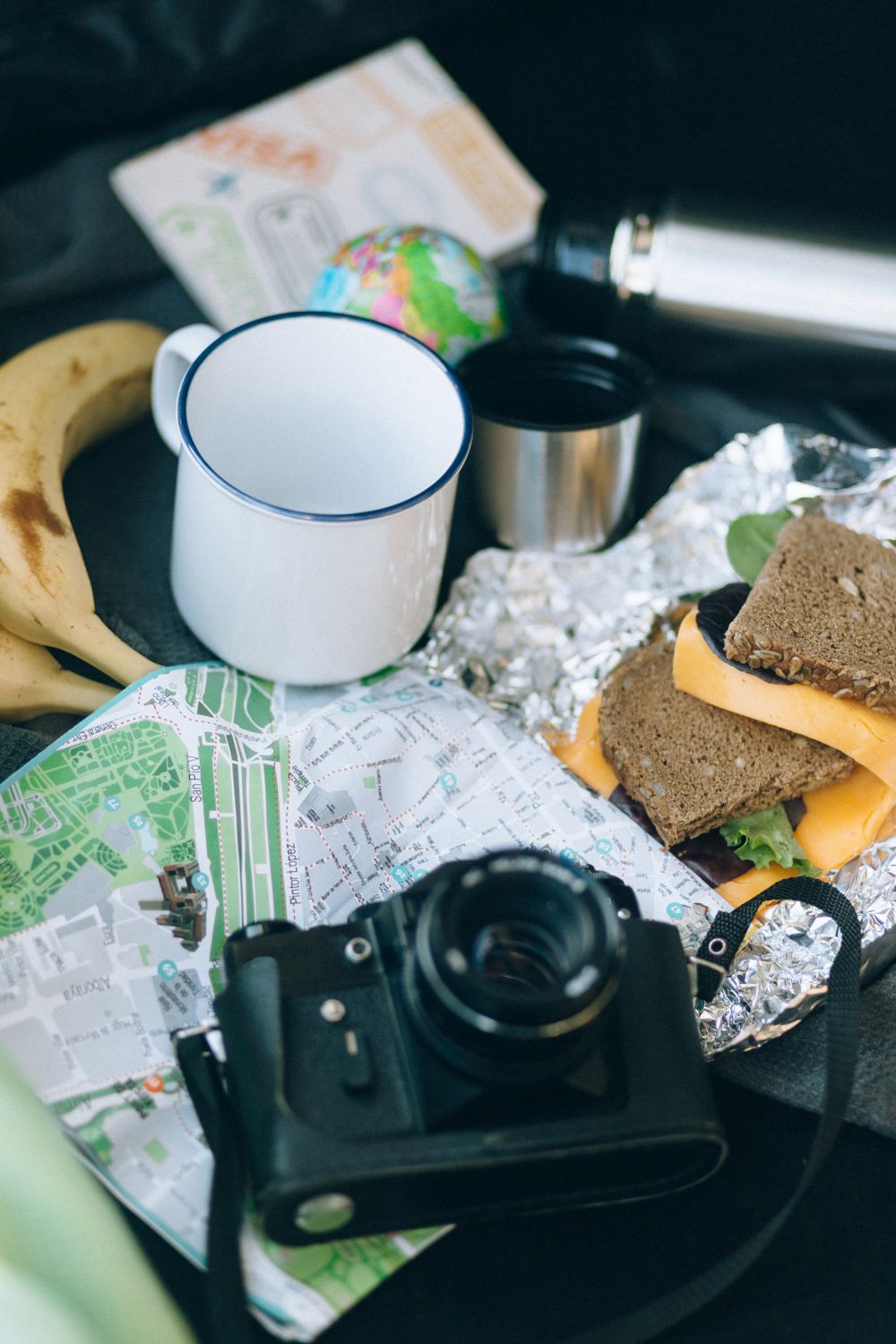 Don’t Let Your Snack Bag Hijack the Vacation: 7 Foods to Rethink Before a Long Road Trip 2 A flat lay of travel essentials including a map, camera, sandwich, and banana for a journey.
