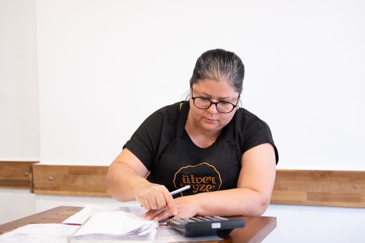 A focused woman uses a calculator and takes notes at a wooden desk in Izmir, Türkiye.