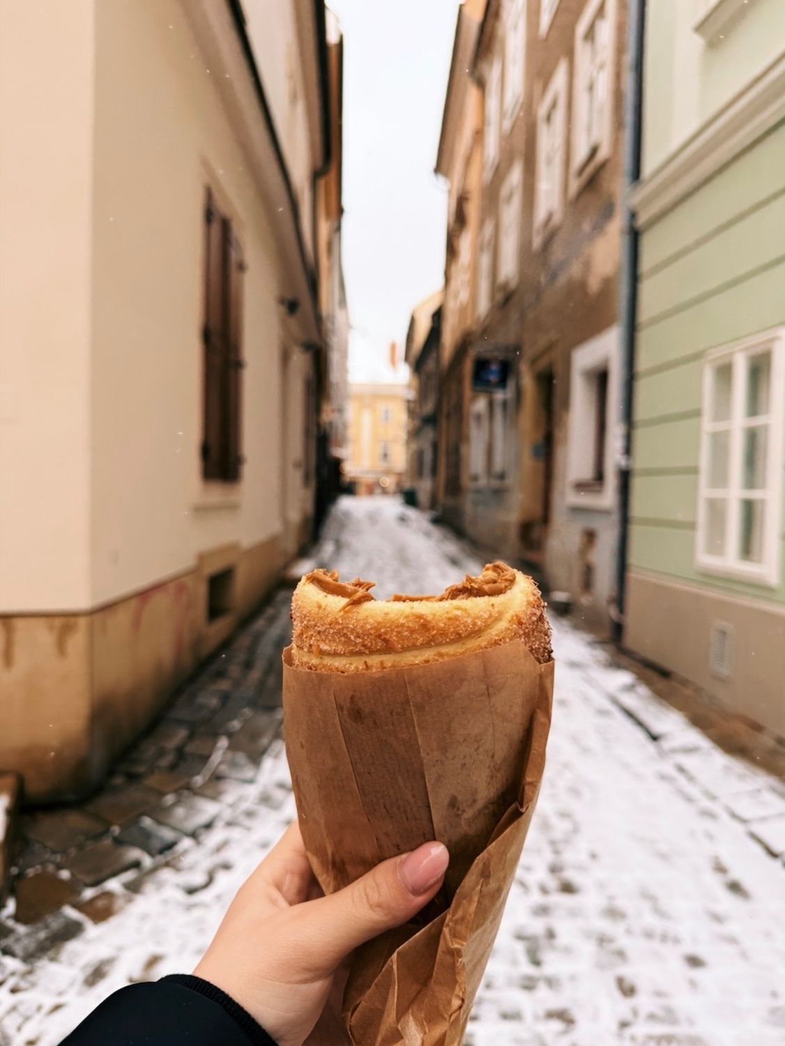 A hand holding a trdelník pastry on a snowy street in Bratislava, Slovakia.