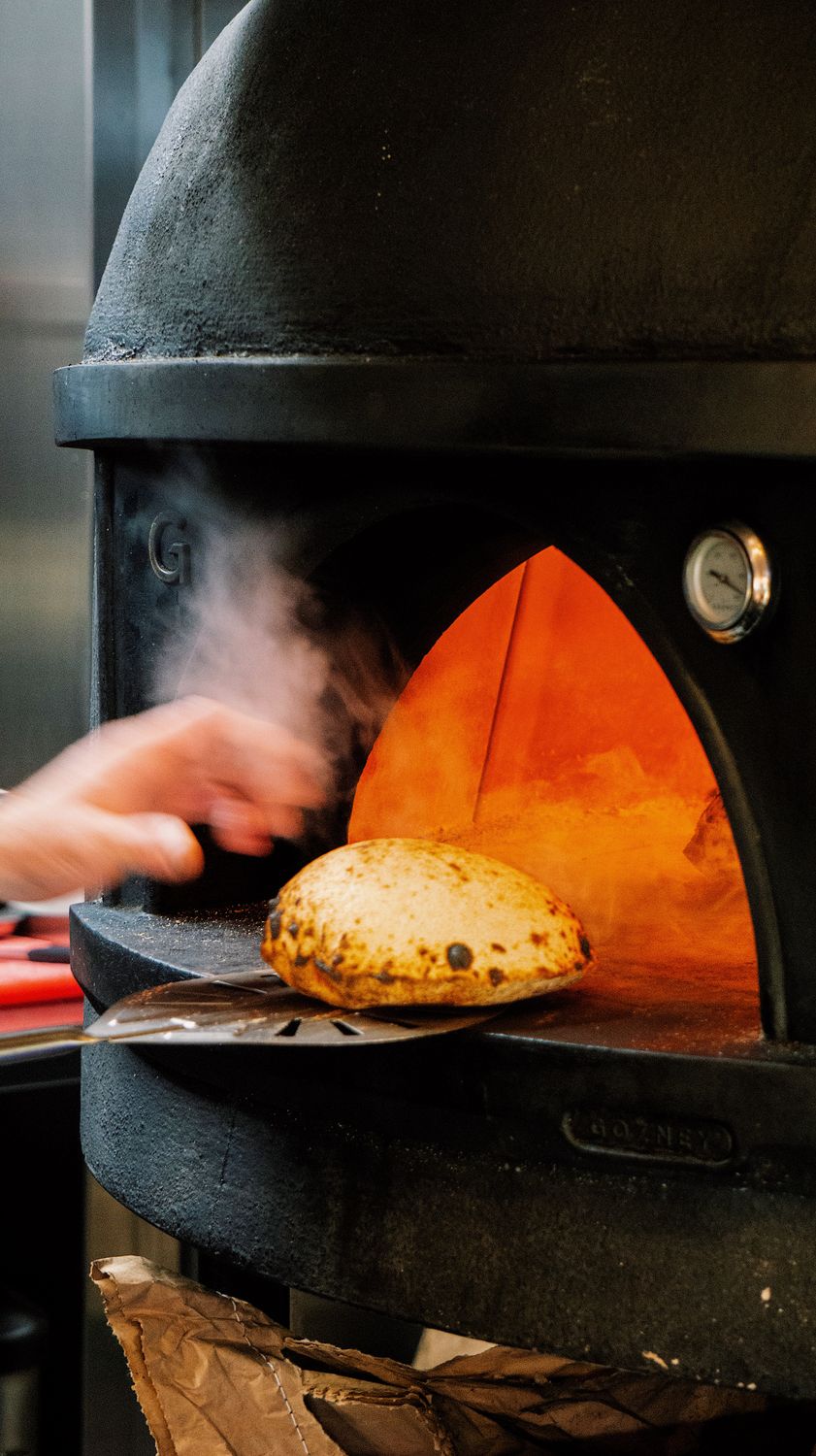 Think You Don’t Like Fennel? A Hot Oven Might Change Your Mind 2 A hand placing freshly baked bread in a traditional wood-fired oven for a perfect crust.
