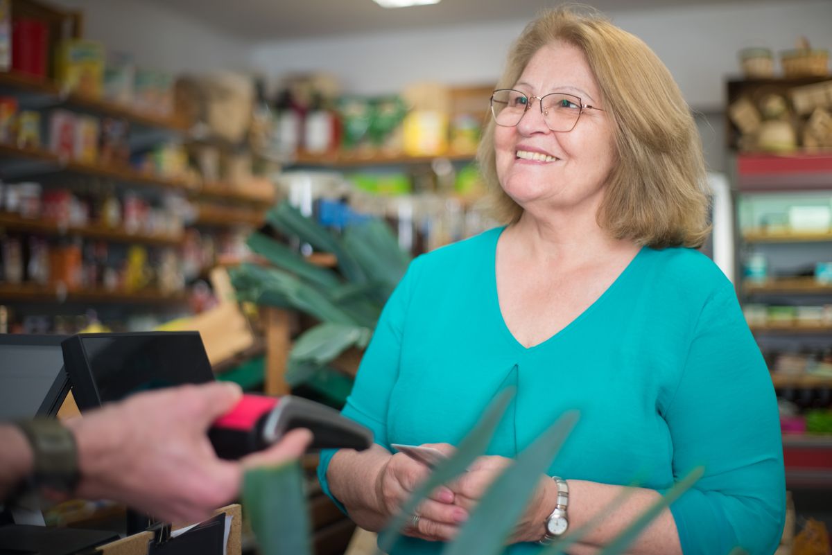 A happy senior woman making a purchase at a local store in Portugal.