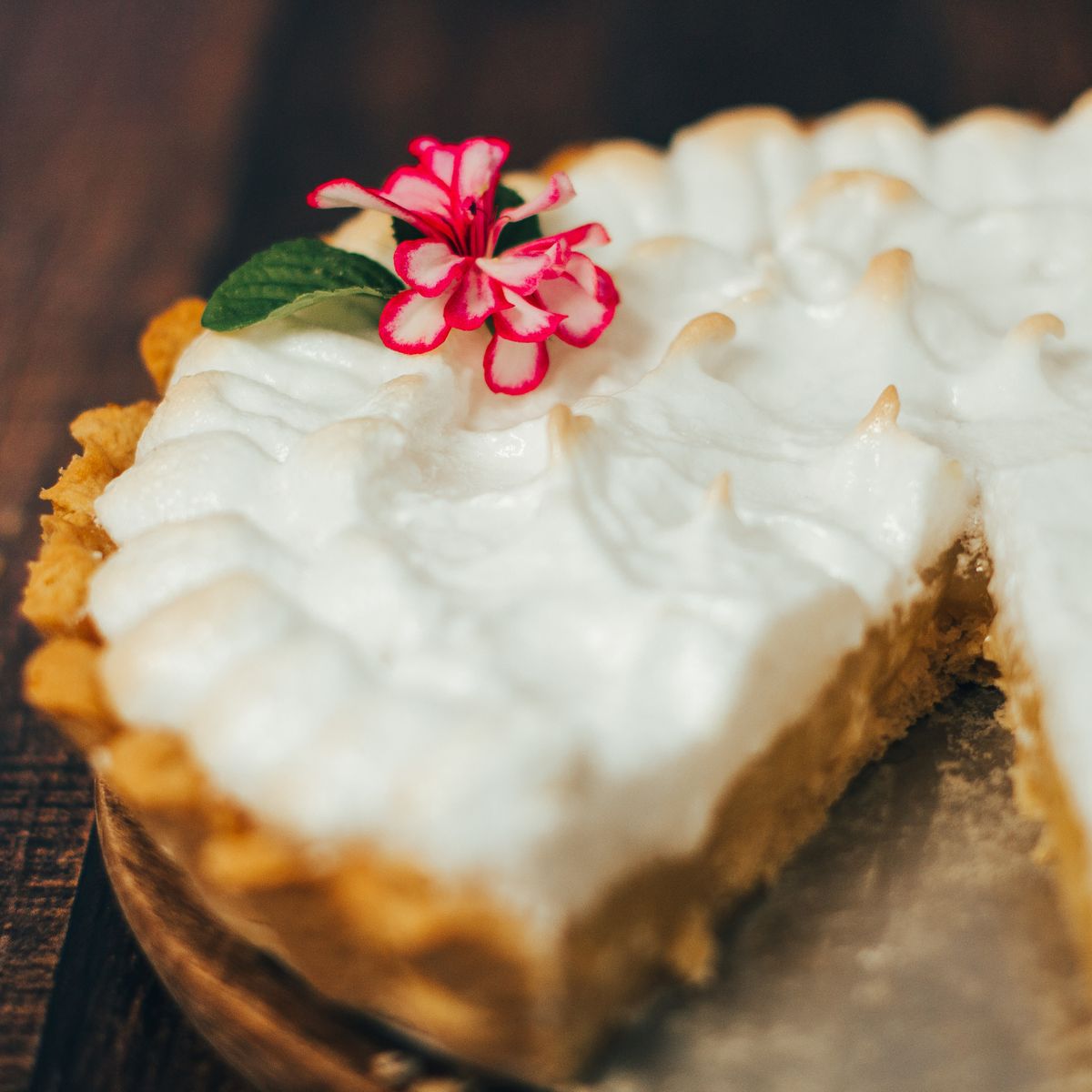 A mouthwatering lemon meringue tart garnished with a vibrant pink flower, perfect for dessert lovers.