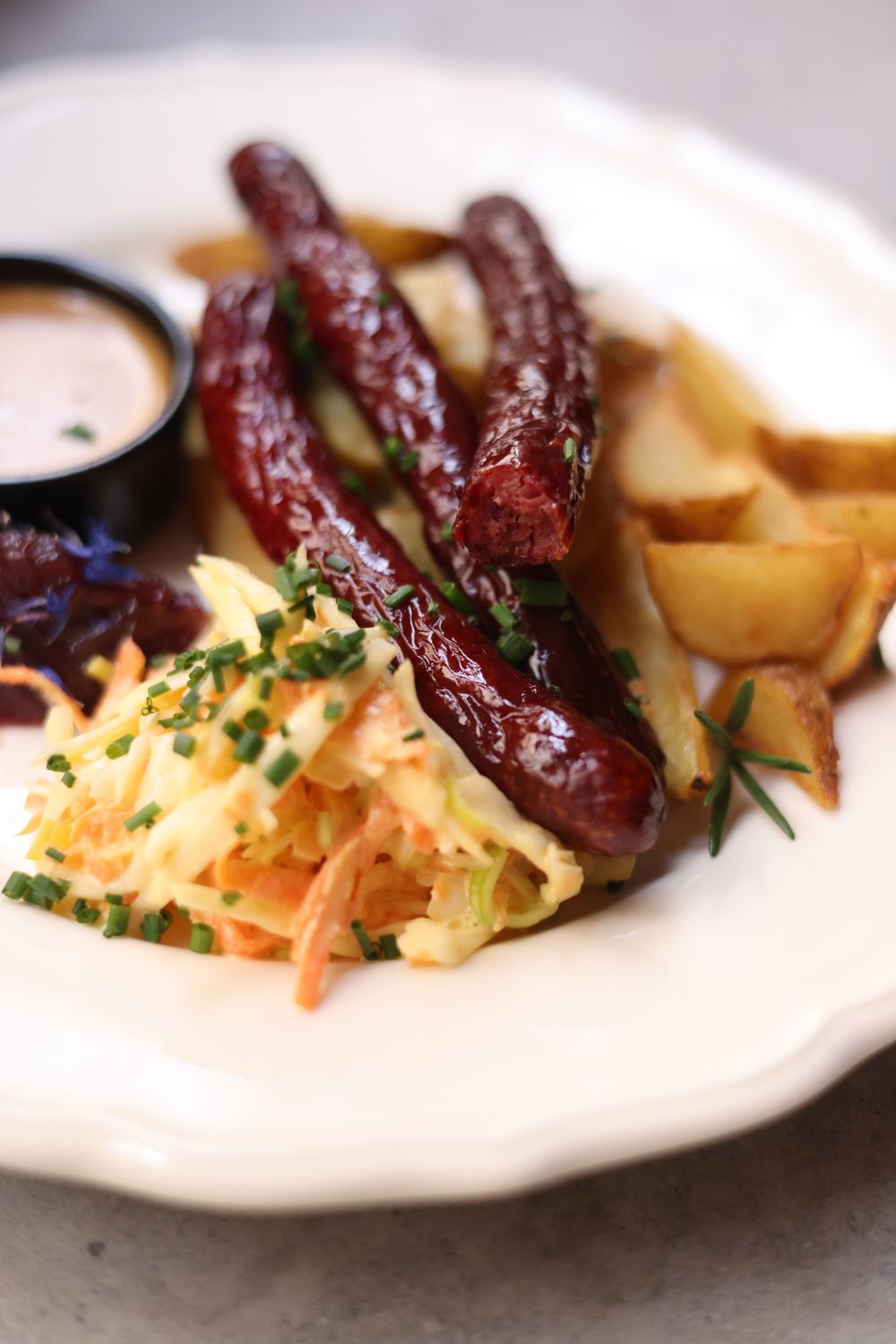 A mouthwatering meal featuring kabanos sausages, coleslaw, and roasted potatoes on a white plate.