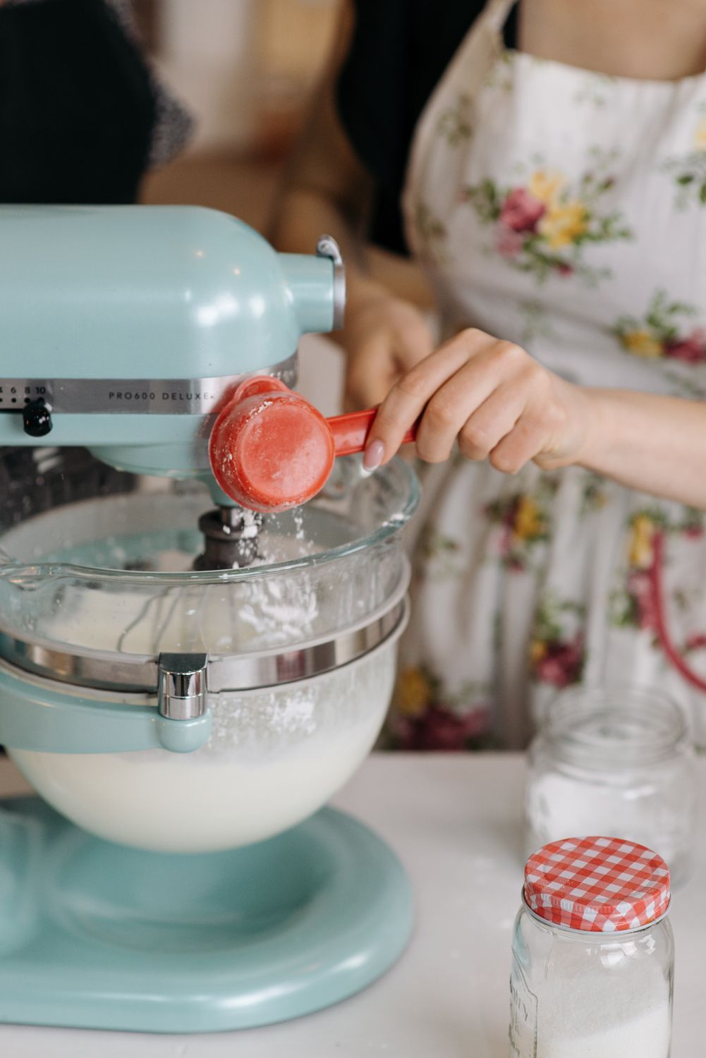 A person adds ingredients to a blue stand mixer while baking indoors.