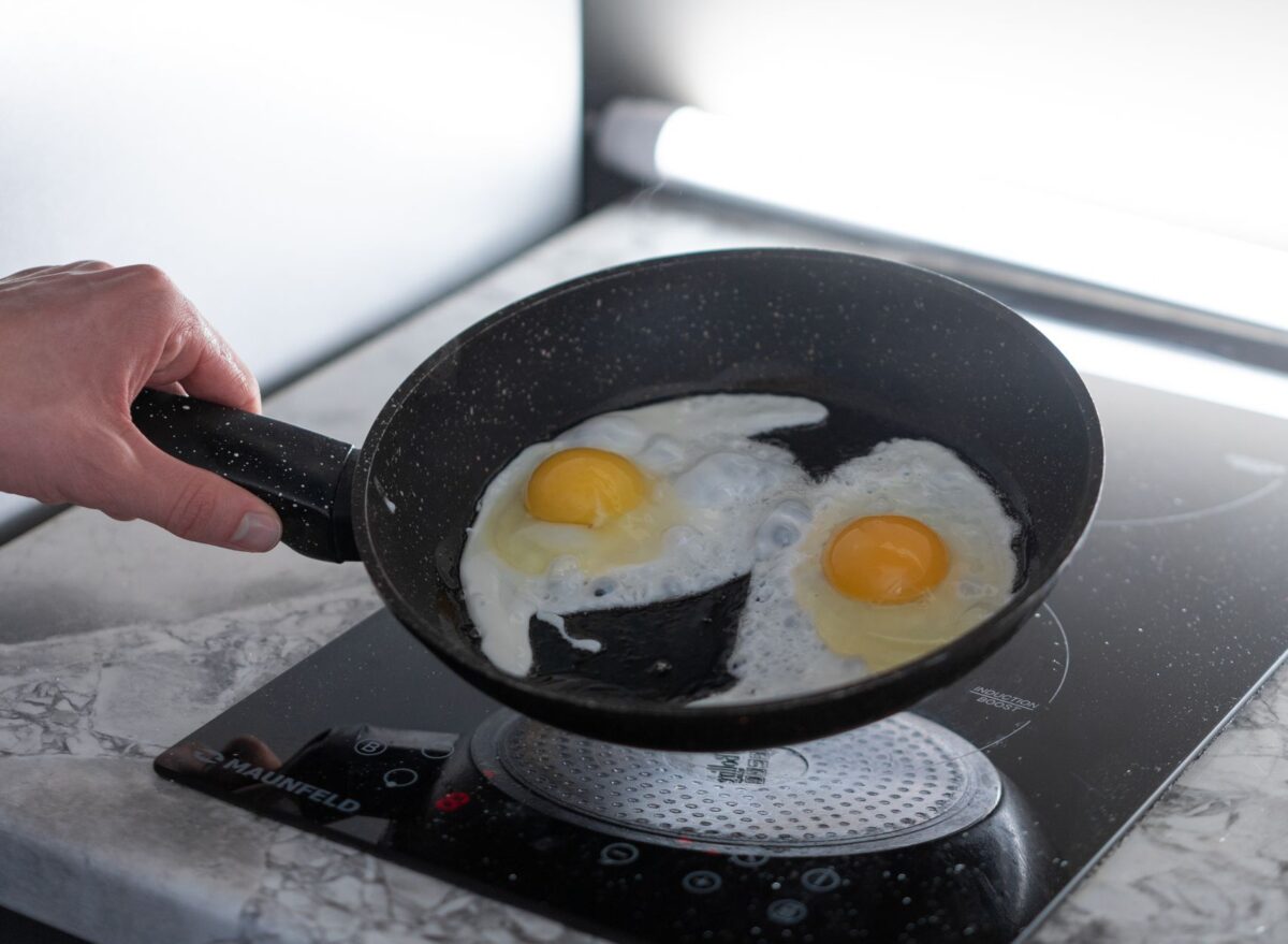 A person frying two eggs in a non-stick pan on an induction stove in a modern kitchen.