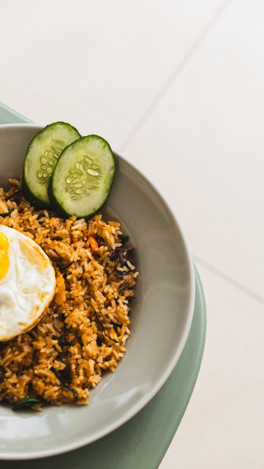A plate of delicious fried rice topped with a sunny-side-up egg and sliced cucumbers.