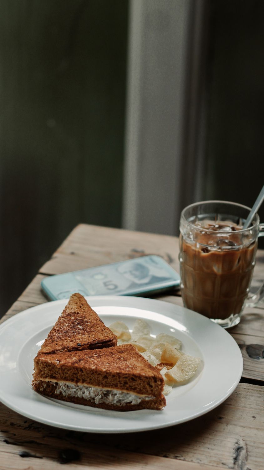 A plate of toast with crisps and iced coffee on a rustic table, perfect breakfast.