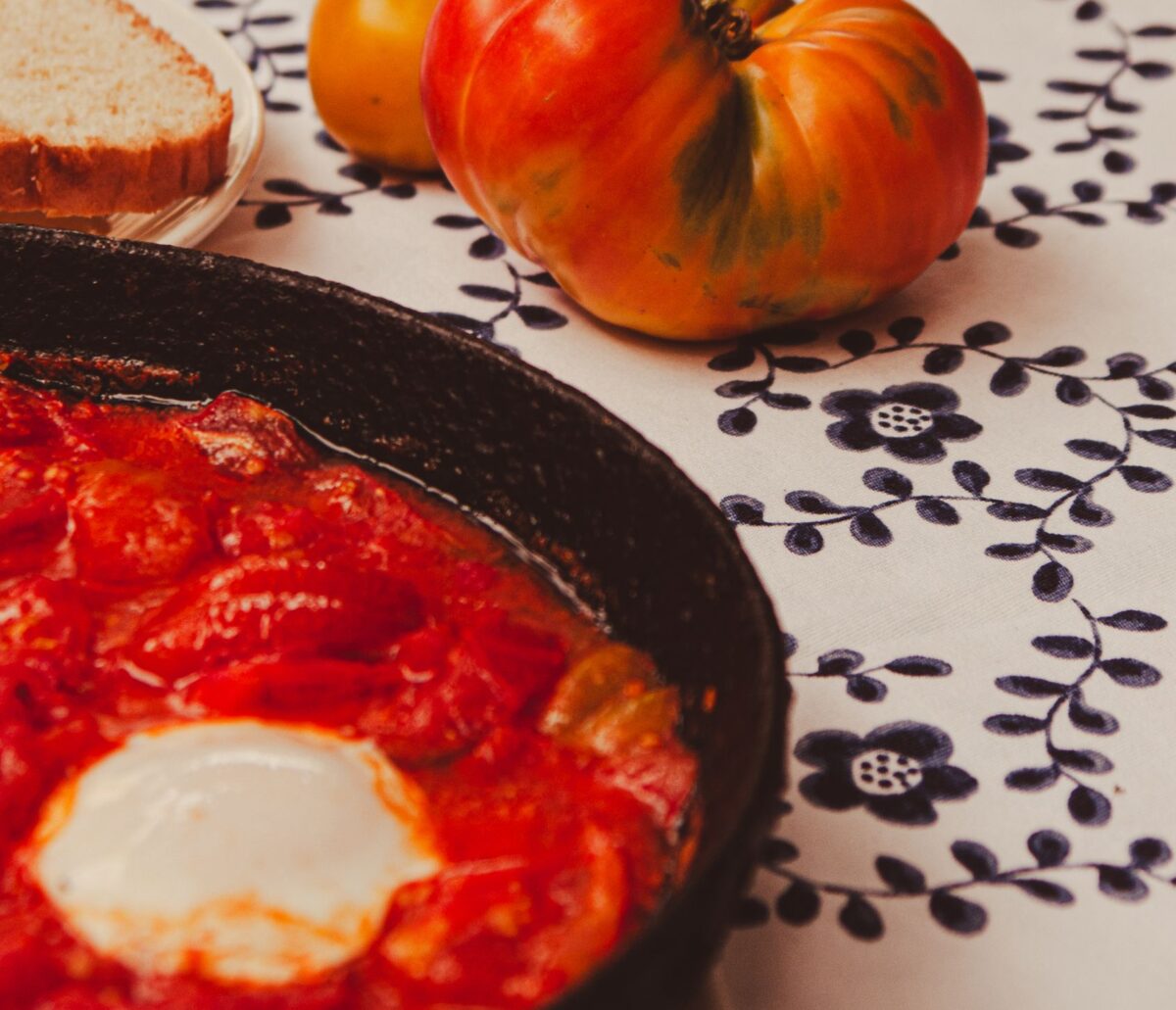 A rustic brunch setting with shakshuka, heirloom tomatoes, and bread on a patterned tablecloth.