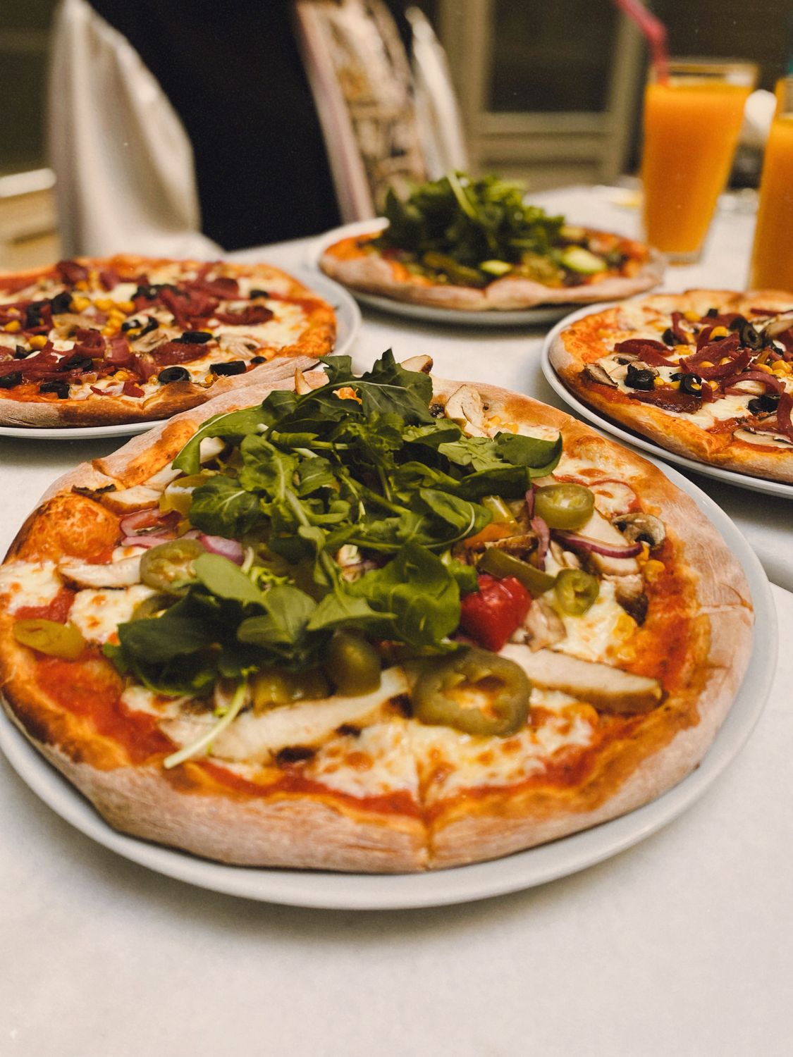 Think You Know Pizza? These 9 Regional Styles Might Start a Delicious Argument 2 A tempting display of four assorted pizzas topped with fresh vegetables and greens, perfect for sharing.