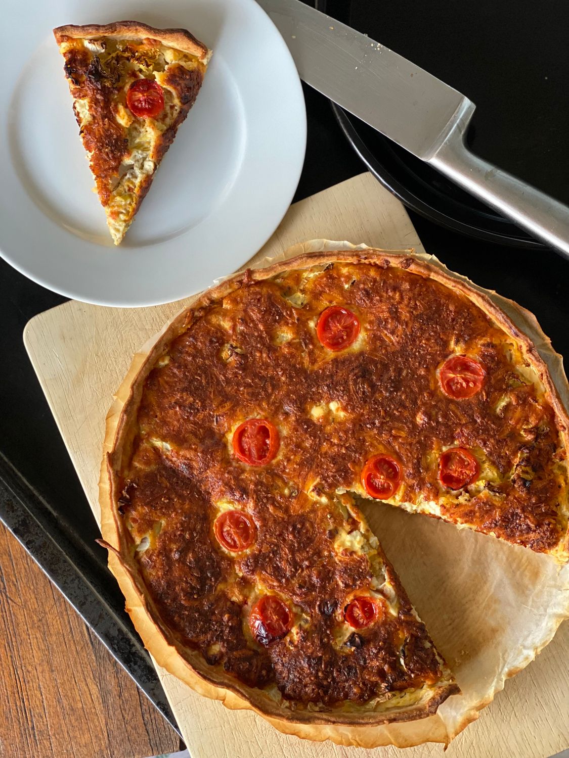 The Secret to a Crisp, Buttery Mushroom and Leek Quiche Starts Before the Filling Goes In 1 A top view of a homemade quiche with cherry tomatoes on a wooden board.