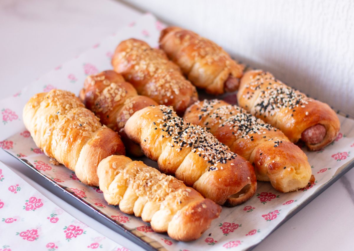A tray of freshly baked sausage rolls with sesame seed toppings, perfect for a snack or breakfast.