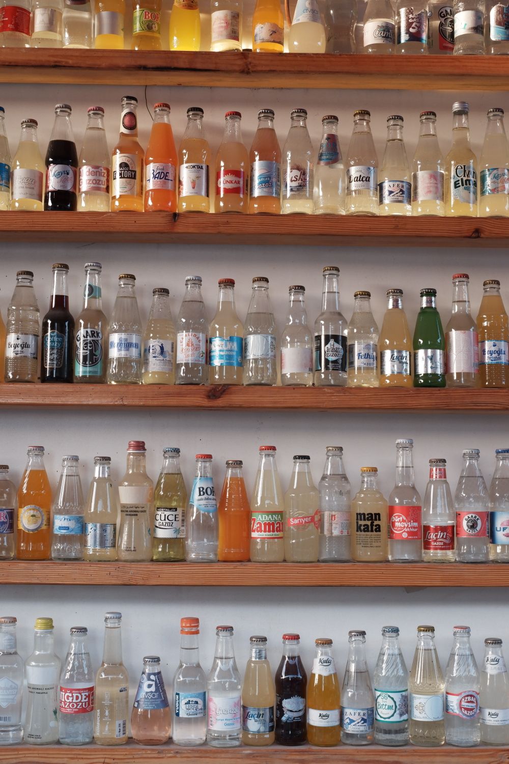 A variety of colorful glass bottles with mixed beverages displayed on wooden shelves, capturing different brands and flavors.