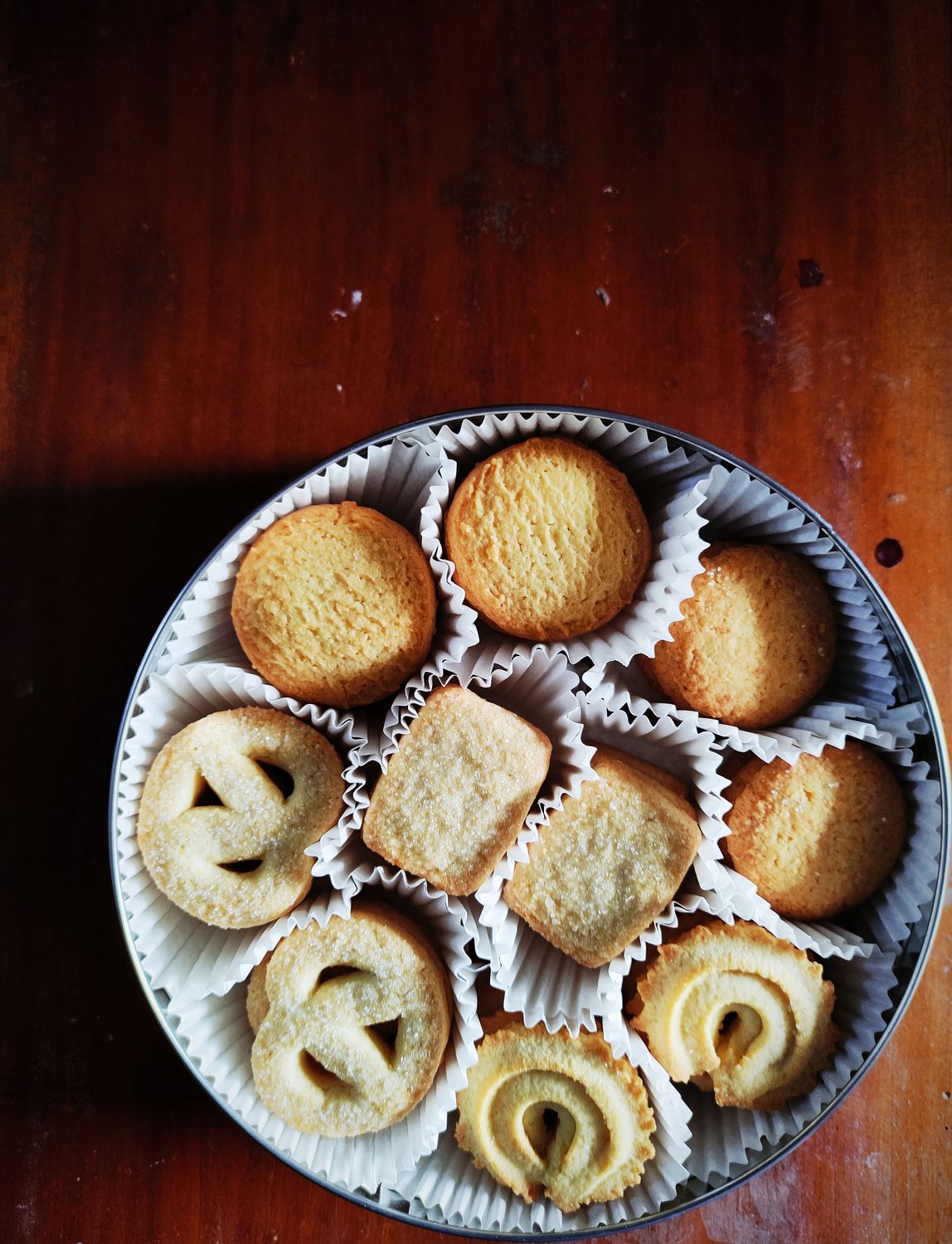 A variety of Danish butter cookies arranged neatly in a round tin box on a wooden table.
