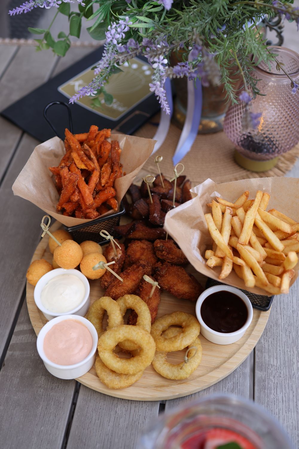 A variety of deep-fried appetizers including onion rings, fries, and sauces served on a wooden platter.
