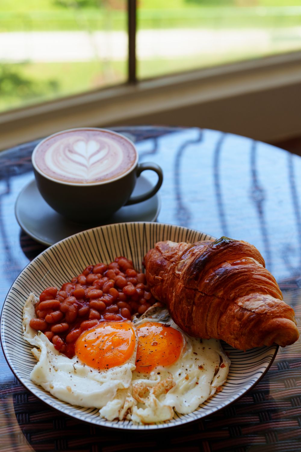 A warm breakfast of eggs, beans, croissant, and coffee with latte art.