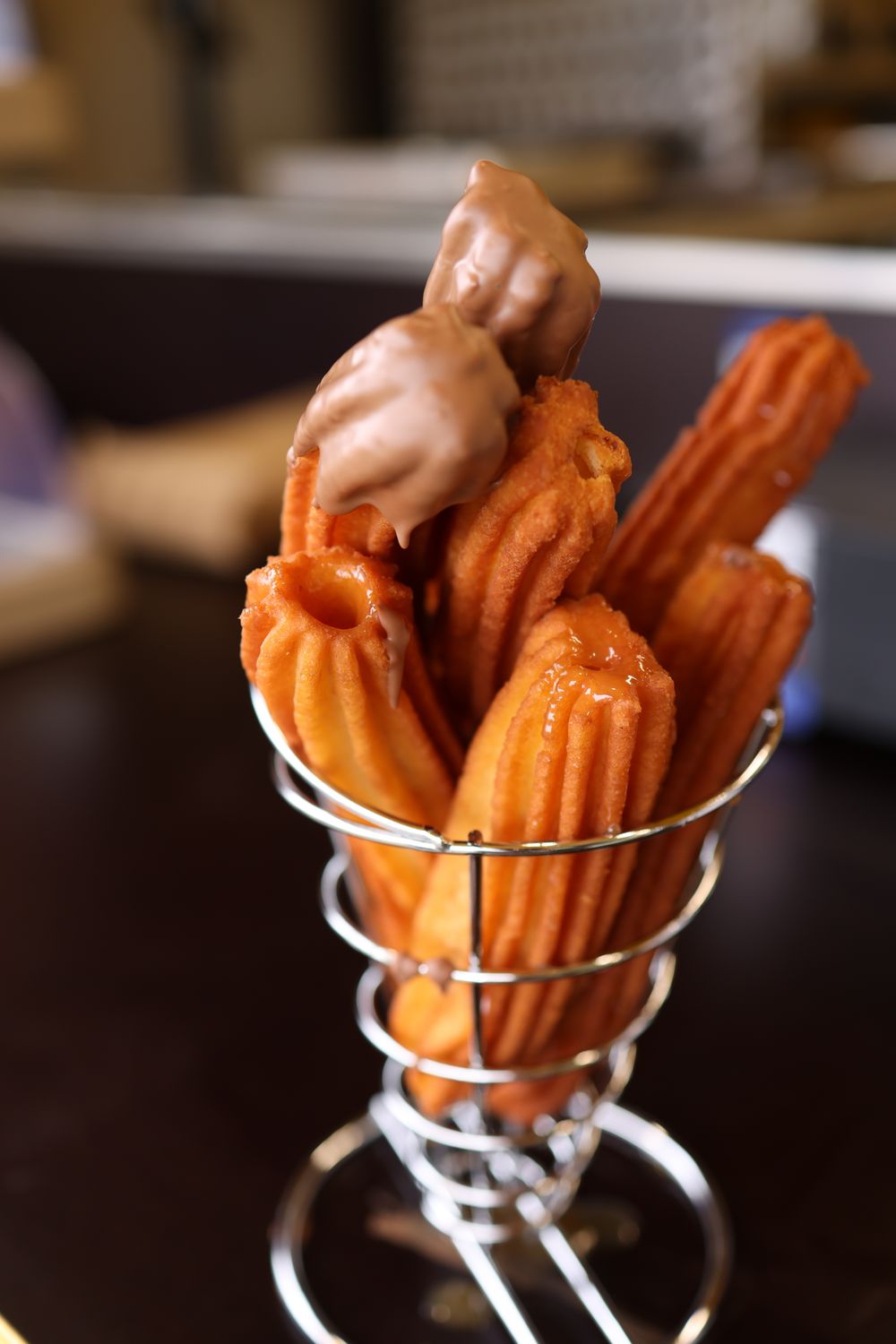 A wire basket filled with freshly made churros topped with chocolate. Perfect for dessert lovers.
