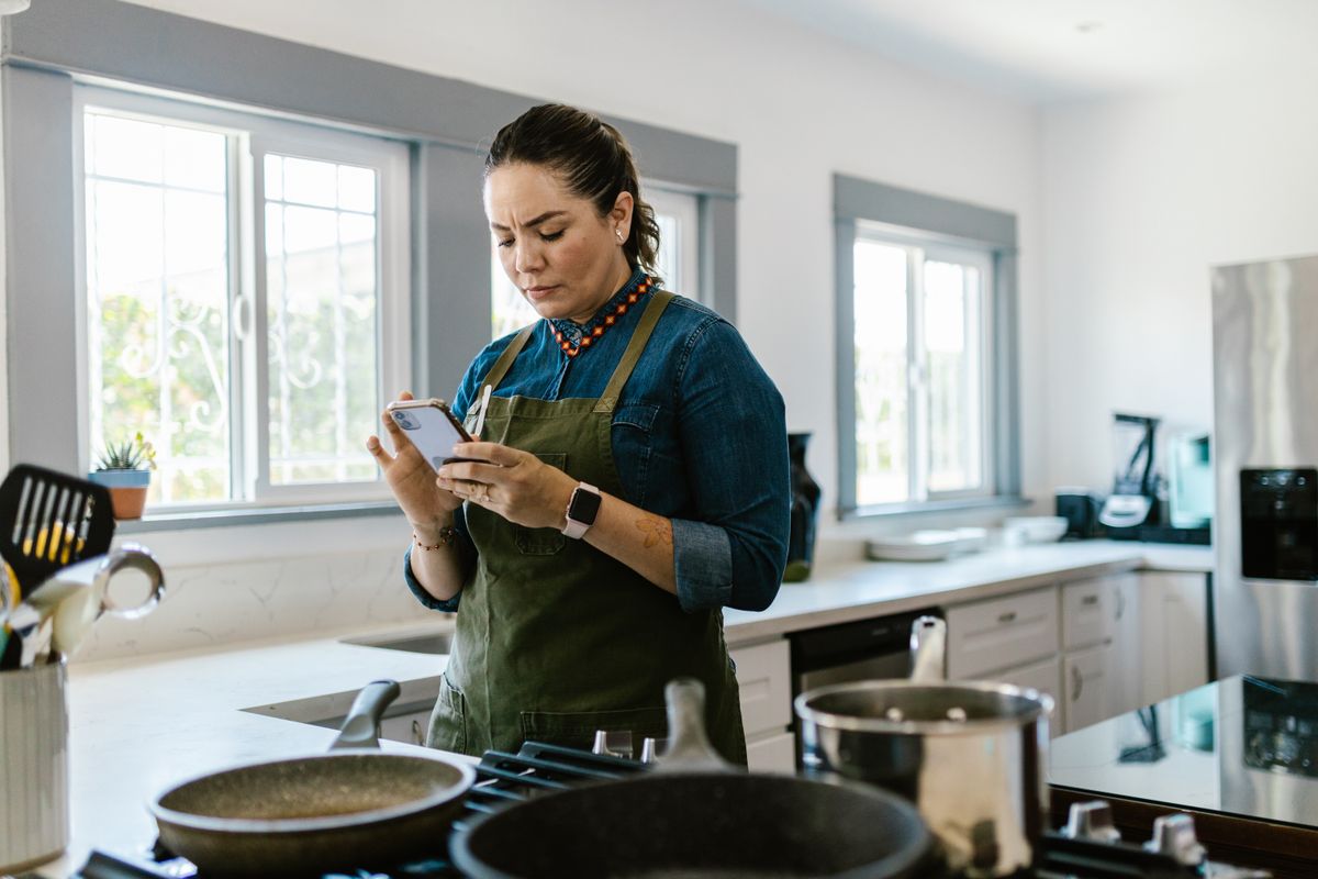 A woman in a modern kitchen following a recipe on her smartphone while cooking.