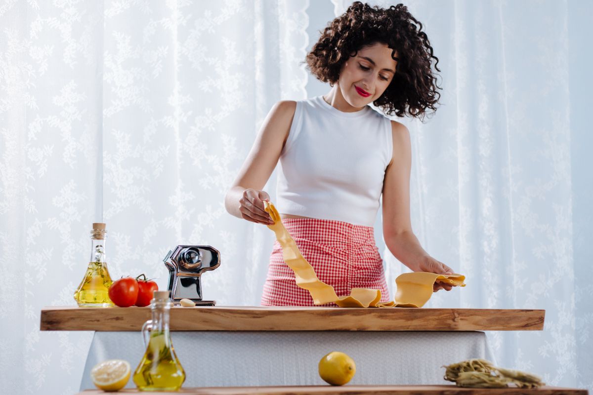 7 Small Additions That Can Make Everyday Food Taste Better 1 A woman joyfully preparing homemade pasta in a bright kitchen setting.