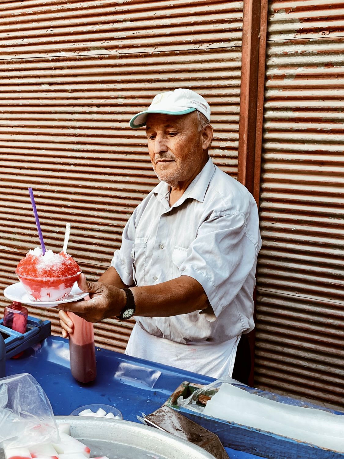 An elderly man vending colorful shaved ice on a street in Adana, Türkiye.