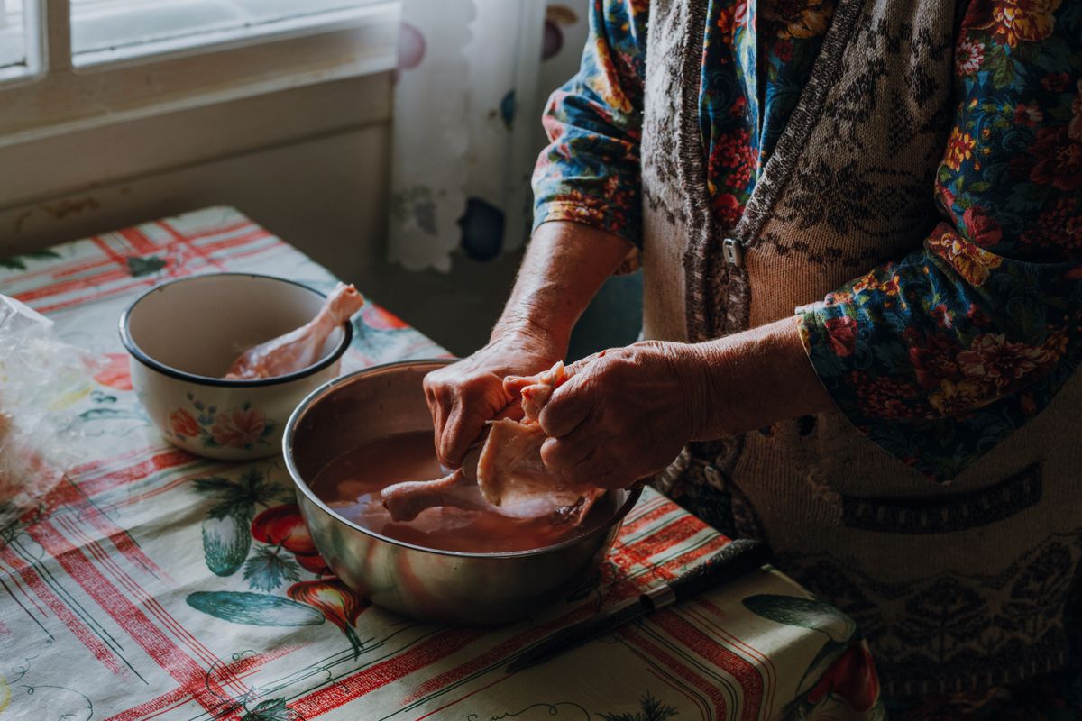 An elderly woman cleaning raw chicken in a kitchen setting, showcasing traditional cooking methods.