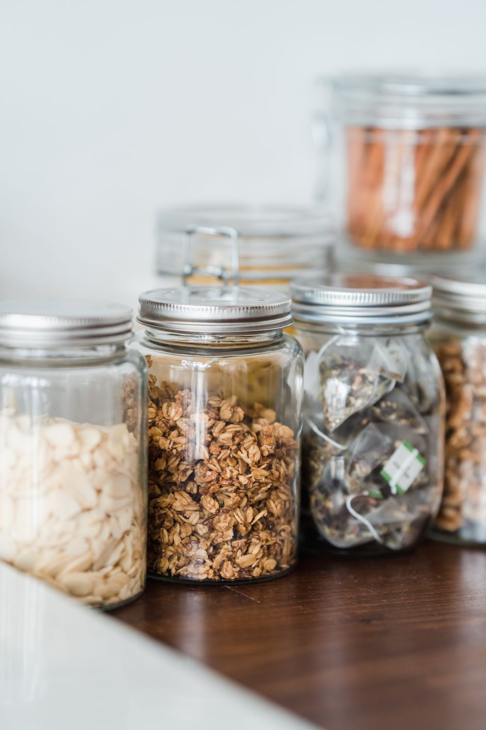 Assorted organic snacks stored in glass jars on a wooden table with a minimalist kitchen theme.