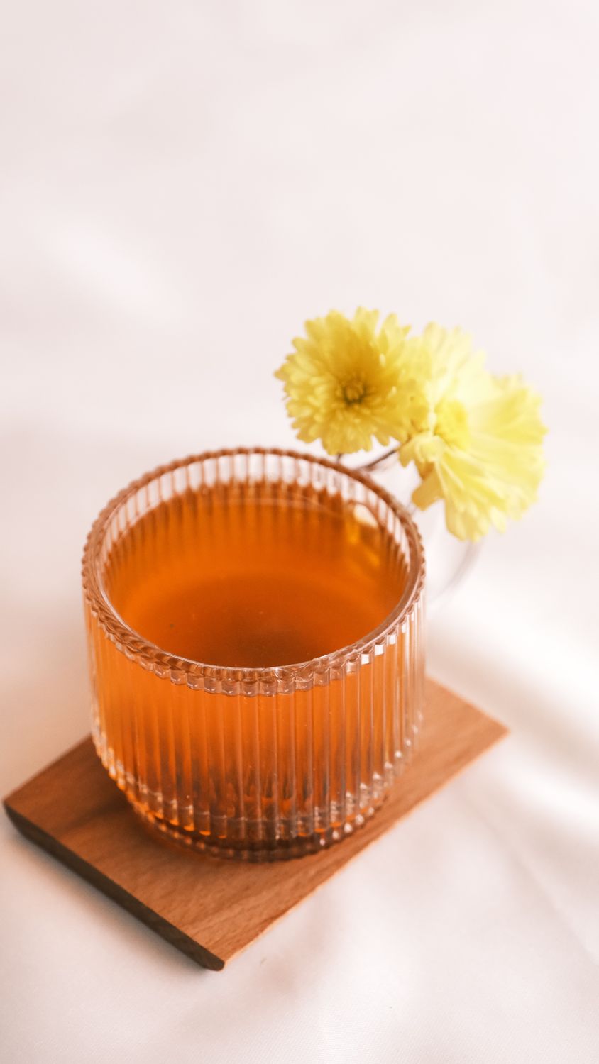 Clear tea cup with yellow flowers on wooden coaster in soft lighting.