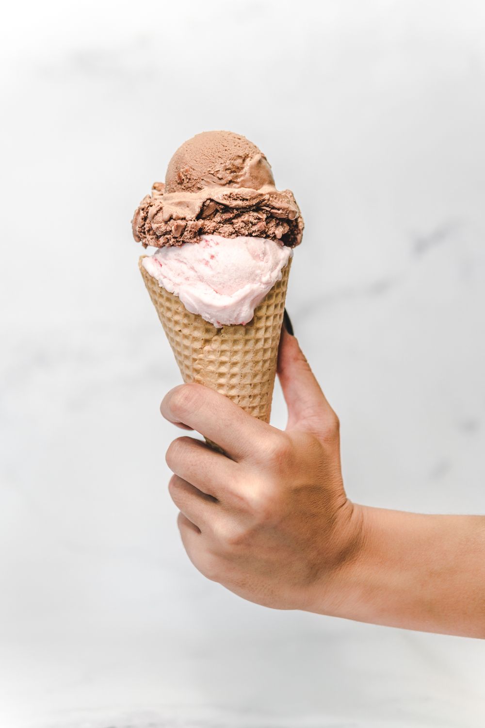 Close-up of a creamy chocolate and strawberry ice cream cone being held.