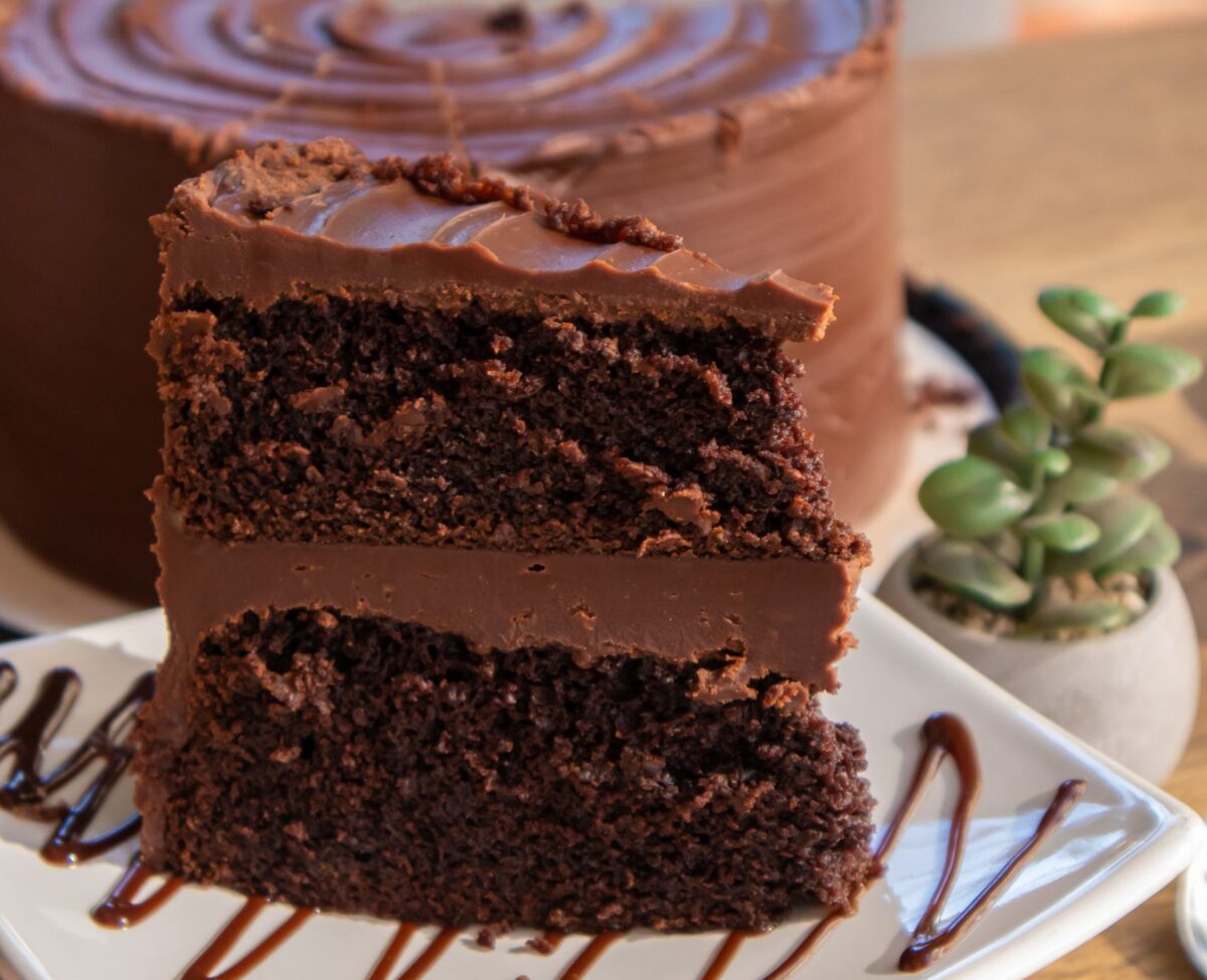 Close-up of a decadent chocolate layer cake slice with frosting on a plate, perfect for dessert lovers.