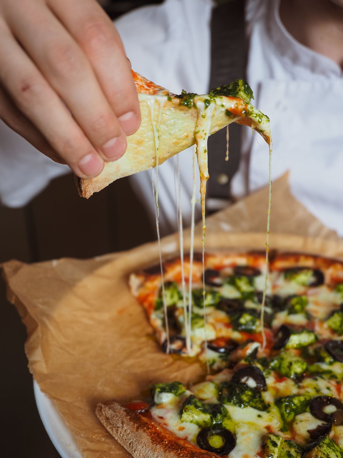 Close-up of a delicious veggie pizza slice with melted cheese and black olives being lifted by hand.