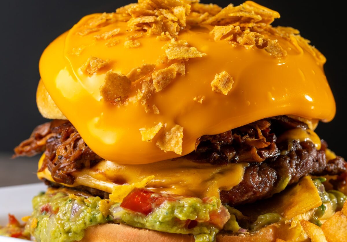 Close-up of a gourmet cheeseburger with guacamole and crispy topping on a platter.