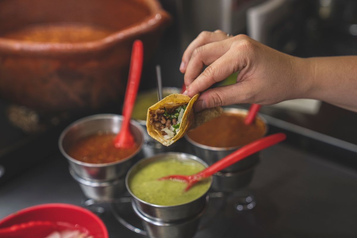 Close-up of a hand holding a taco with various sauces, capturing the essence of Mexican street food.