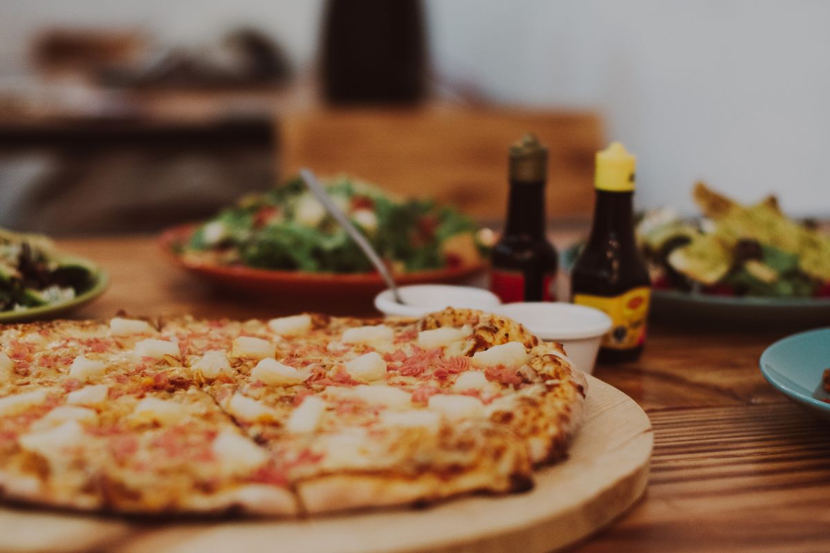 9 Pizza Toppings That Divide America 1 Close-up of a tasty Hawaiian pizza with pineapple and ham toppings on a wooden table.