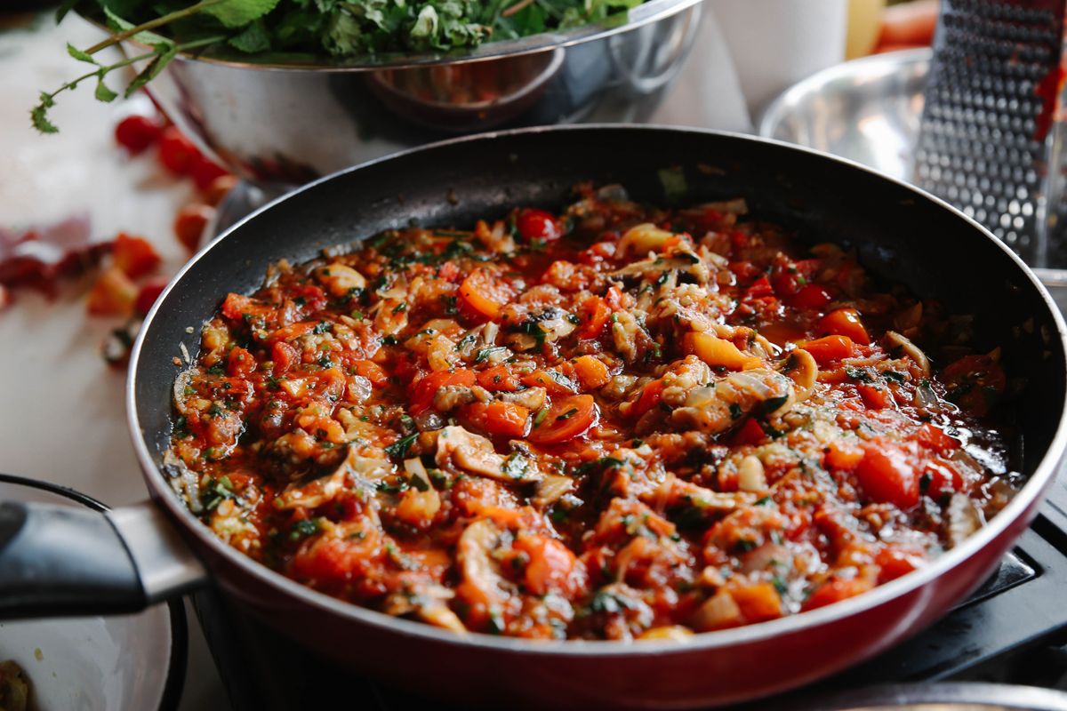 Close-up of a vibrant ratatouille dish cooking in a pan, featuring tomatoes and herbs.