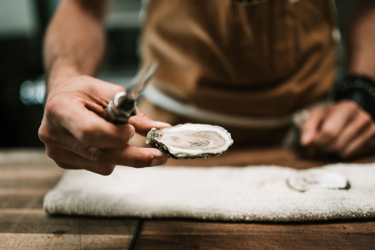 Close-up of chef's hand shucking an oyster on a wooden table in the kitchen.