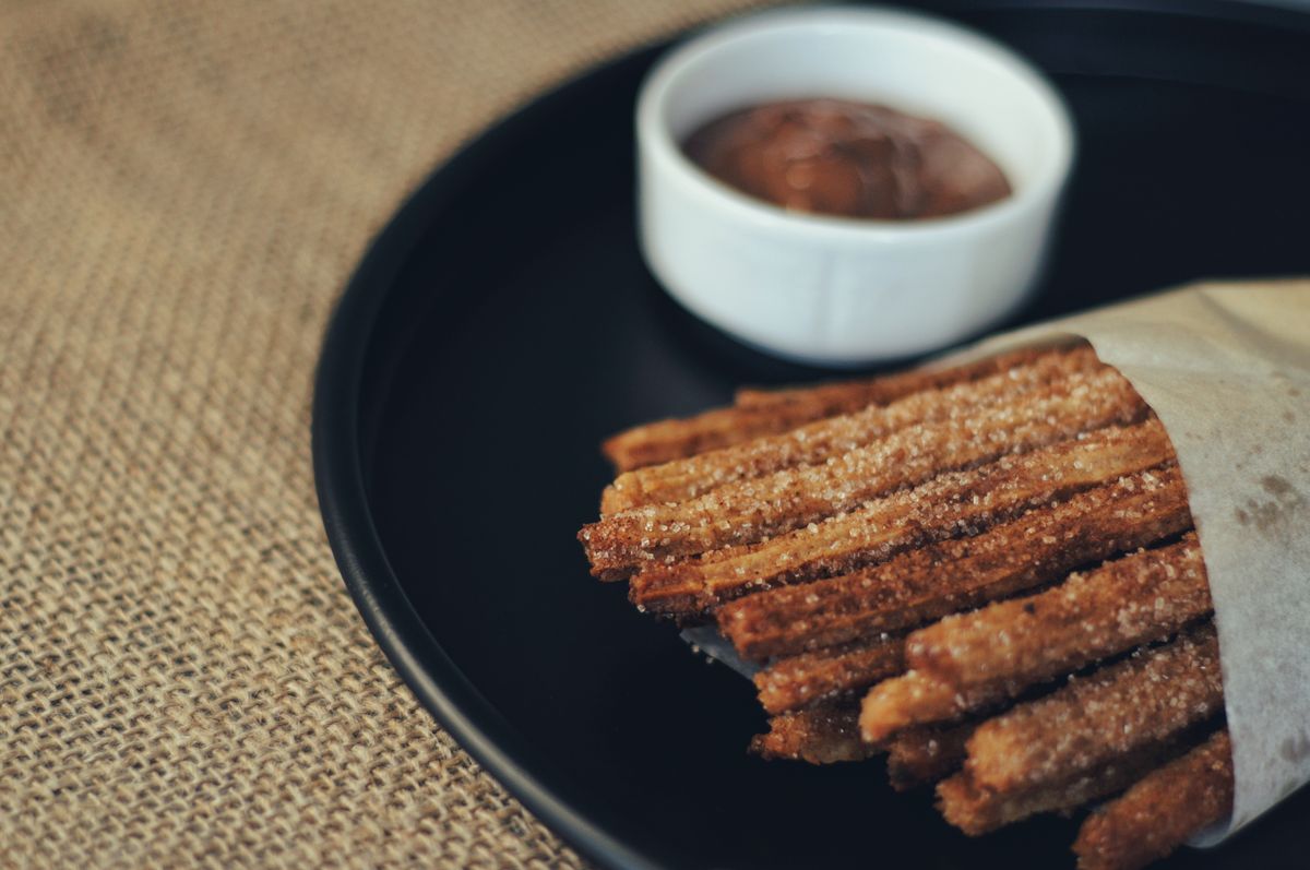Close-up of cinnamon churros served with a chocolate dip on a dark plate.