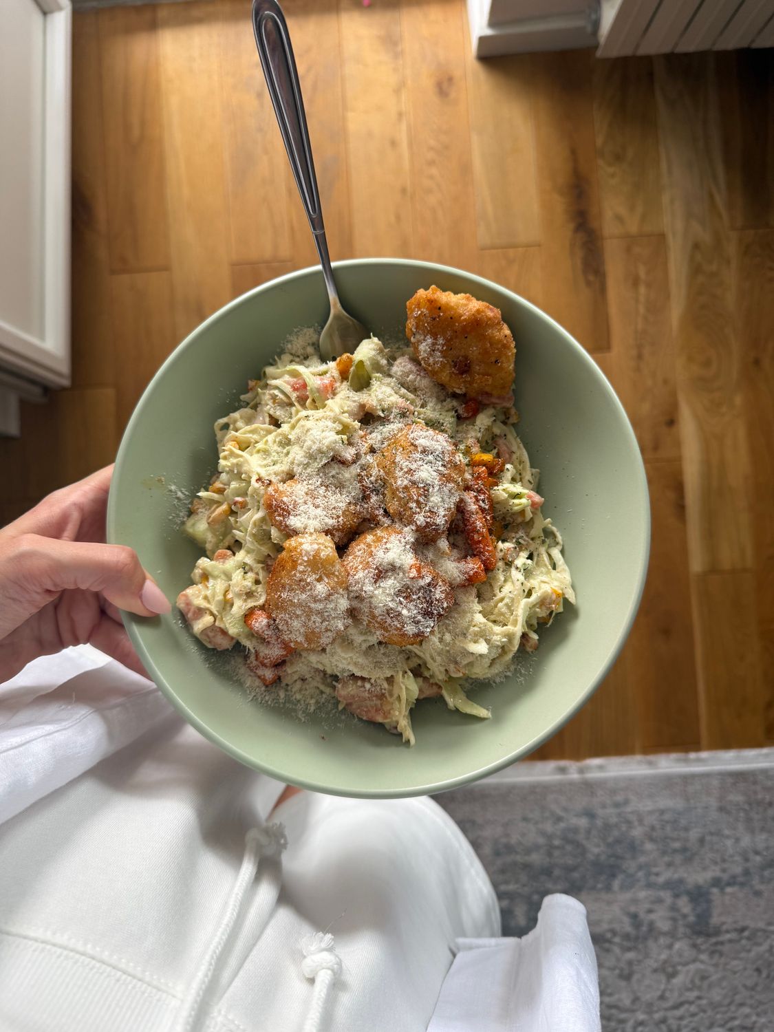 Close-up of creamy chicken pasta topped with crispy nuggets and parmesan cheese.