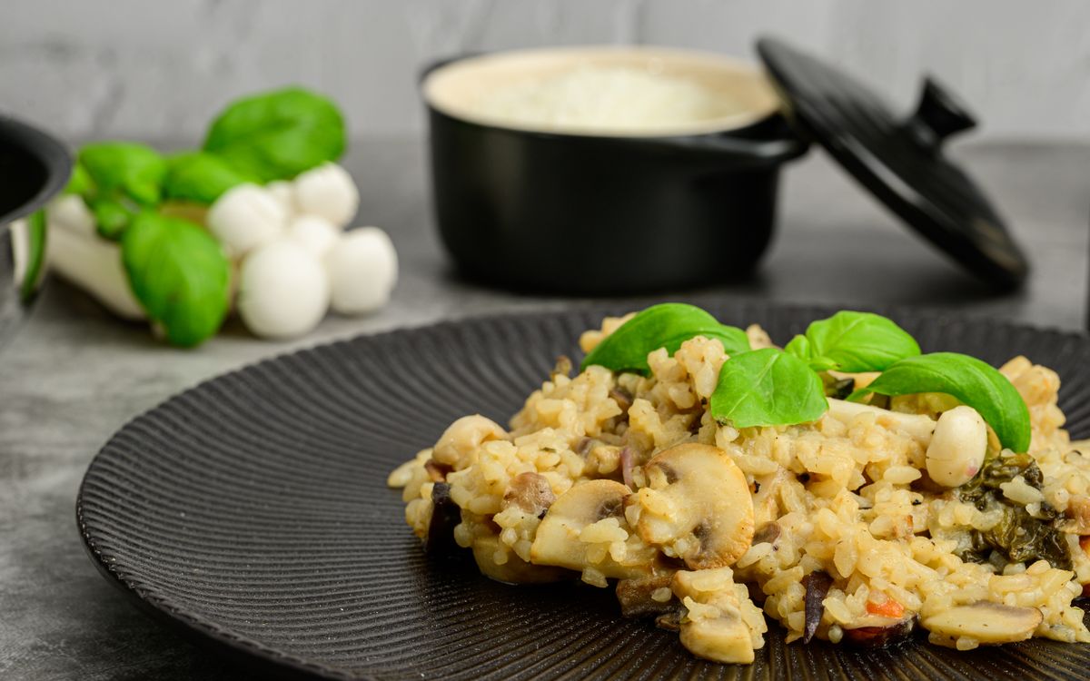 5 Rice Dishes That Put White Wine to Good Use 1 Close-up of creamy mushroom risotto topped with basil on a black plate, perfect for foodies.