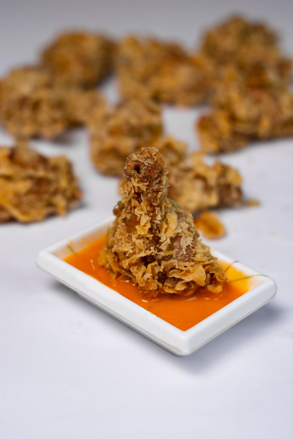 Close-up of crispy fried chicken leg on white plate with tangy orange sauce.