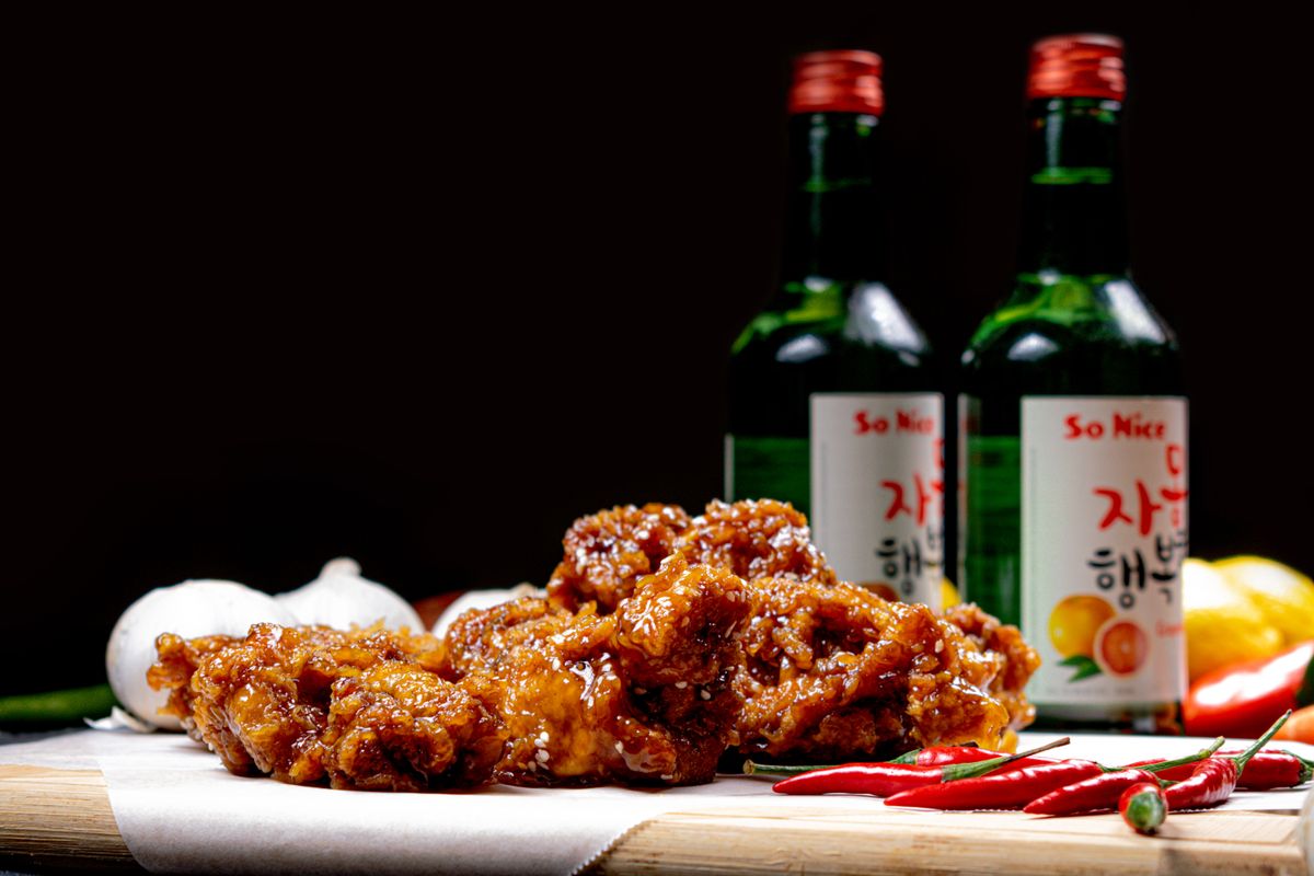 Those Little Dishes Aren’t Just Extras: What Makes a Korean Table So Special 2 Close-up of crispy fried chicken with soju bottles and chili peppers on a rustic table.