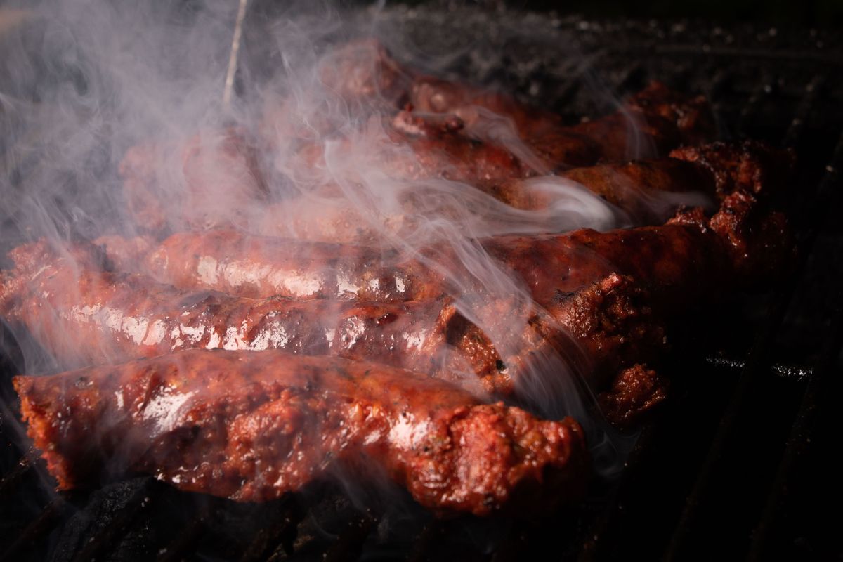 Close-up of delicious sausages grilling on BBQ with smoke rising.