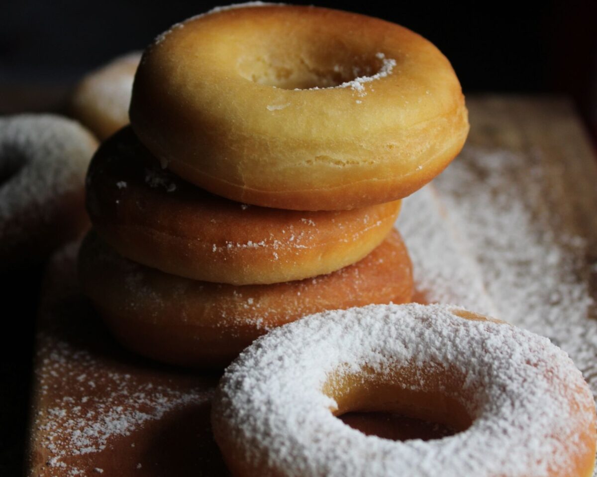 9 Grocery Store Bakery Items Ranked From Worst to Best 1 Close-up of fresh donuts dusted with powdered sugar, stacked on a wooden board.