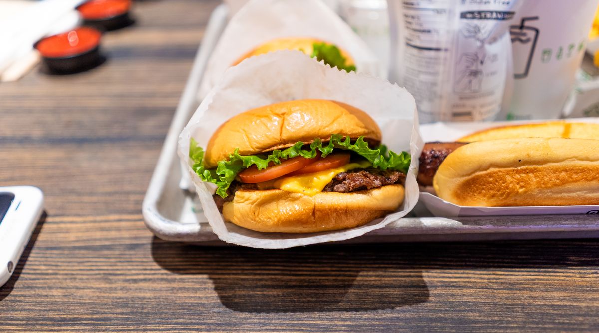 Close-up of freshly prepared cheeseburgers with lettuce and tomato on a metal serving tray.